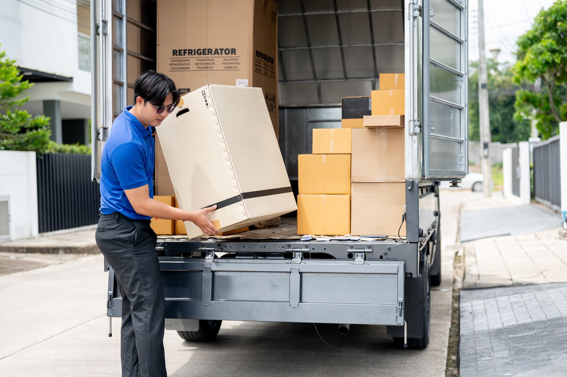 An Asian delivery man or mover is unloading cardboard boxes from his truck.